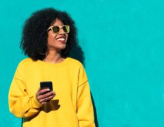 Woman wearing a yellow jumper and holding a phone posing against an aqua background