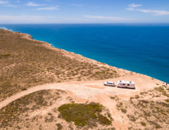 Aerial view of a caravan and car on a desert road near the ocean.