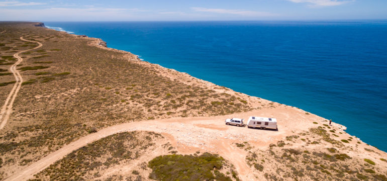 Aerial view of a caravan and car on a desert road near the ocean.
