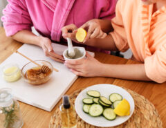 Two people in robes crushing lemons and cutting cucumbers on a wooden table